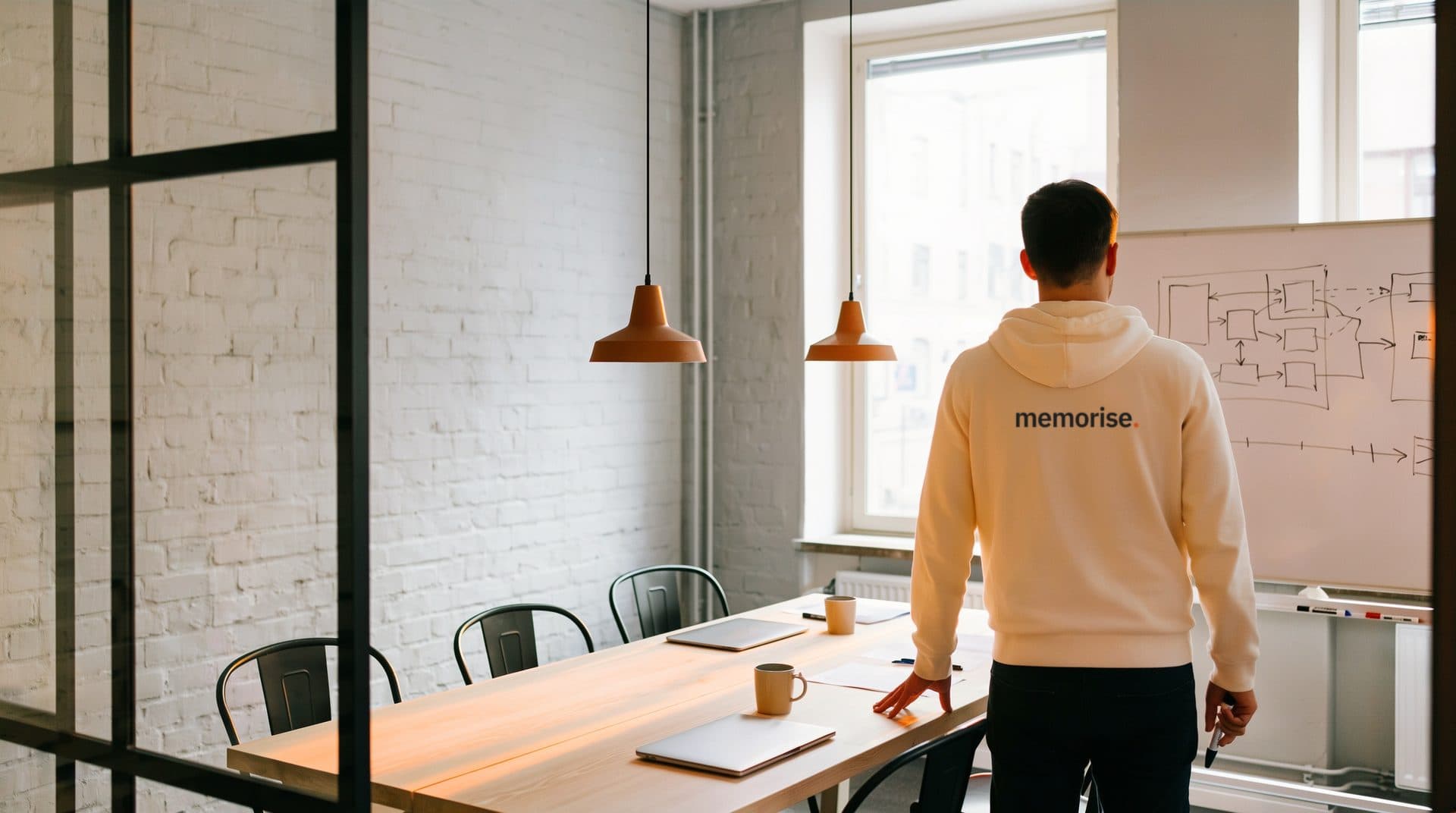 Person i Memorise-hoodie står vid kortänden av ett mötesbord framför en whiteboard med en plan i rutor och pilar