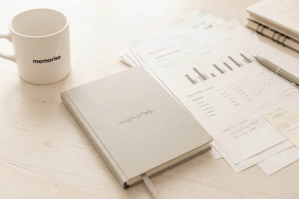 Extern marknadschef-analys på skrivbord med memorise-kaffekopp, svart anteckningsbok och KPI-dokument med diagram