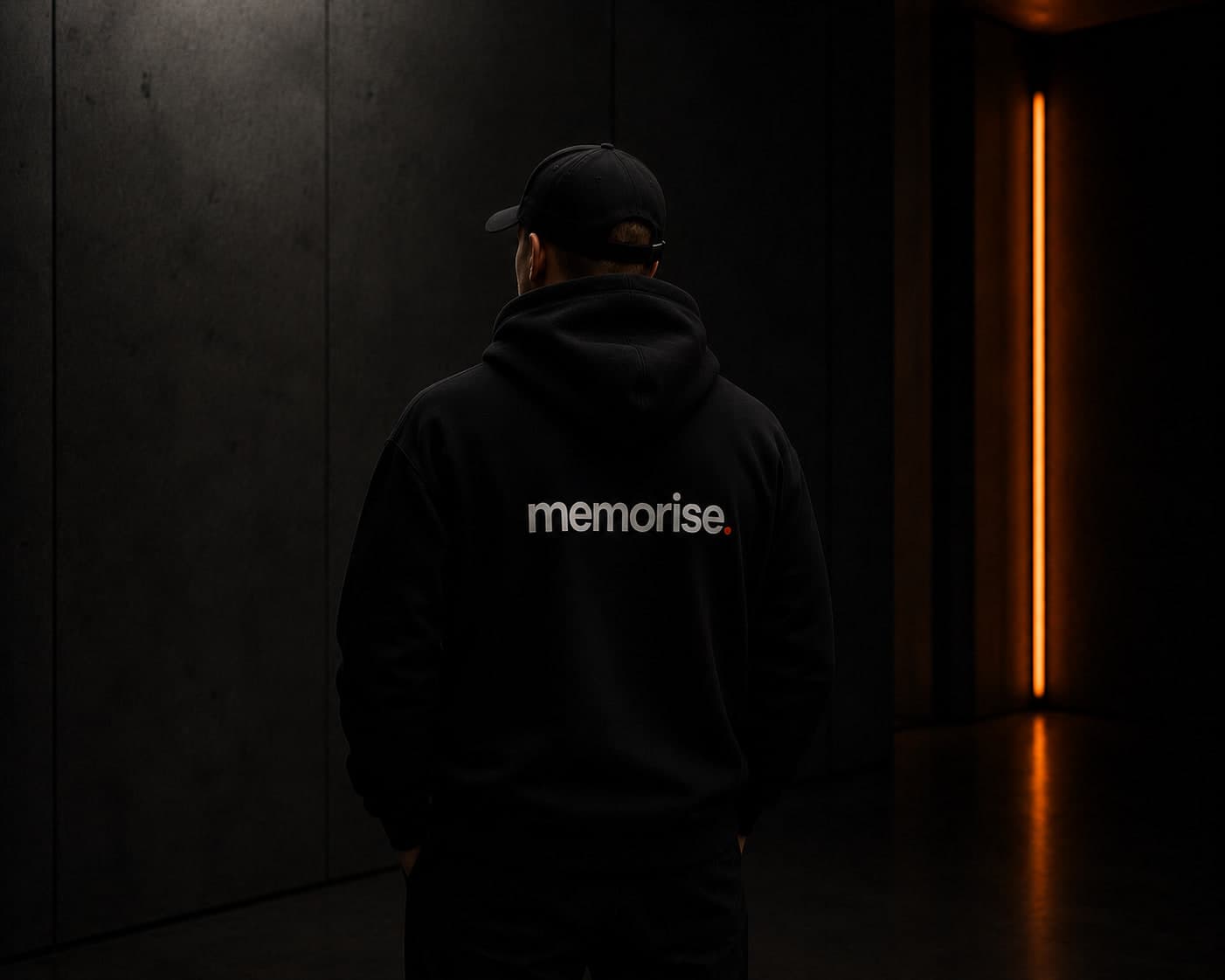 Memorise specialist seen from behind in cap and hoodie against dark wall with warm orange light bar