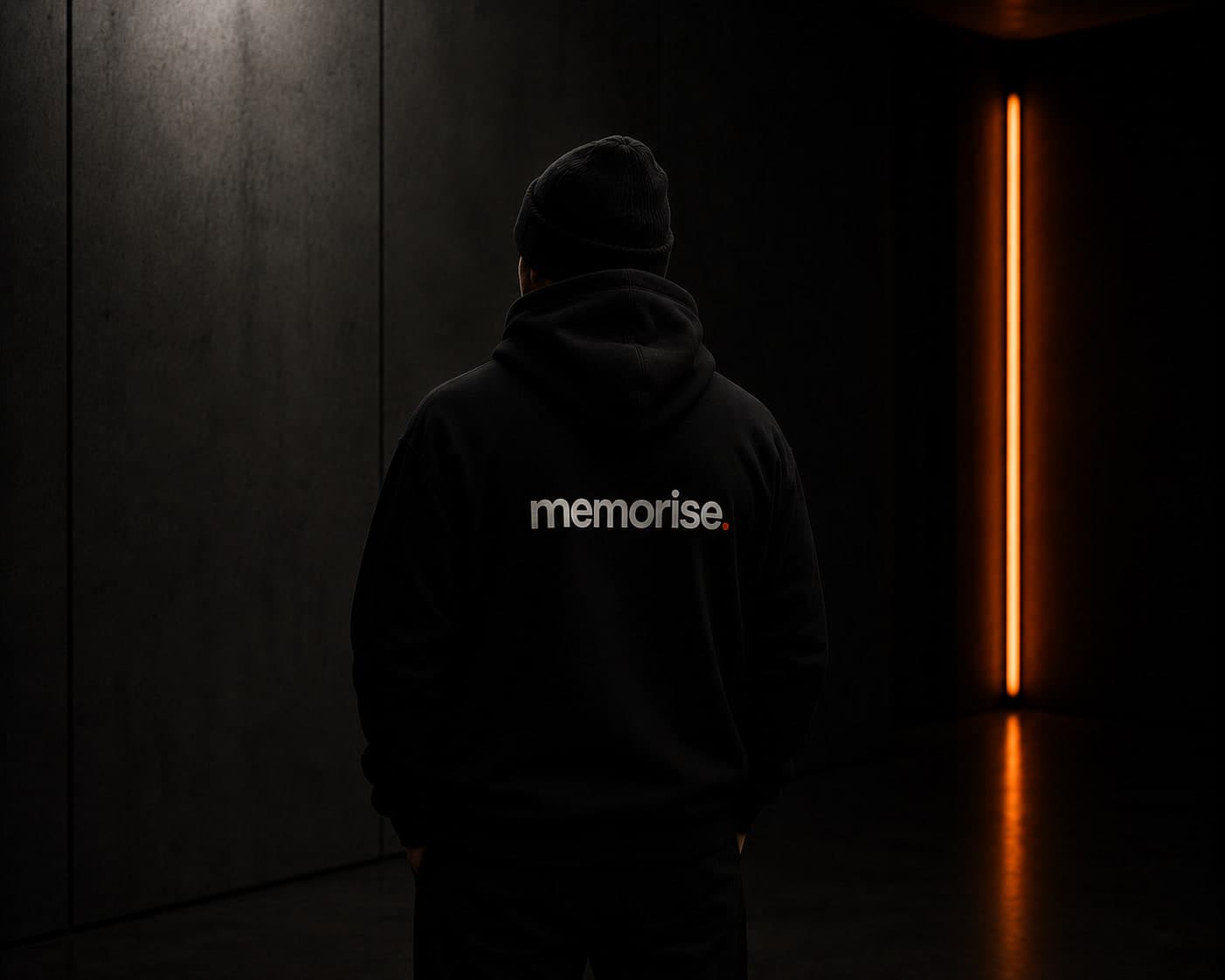Memorise specialist seen from behind in beanie and hoodie against dark wall with warm orange light bar